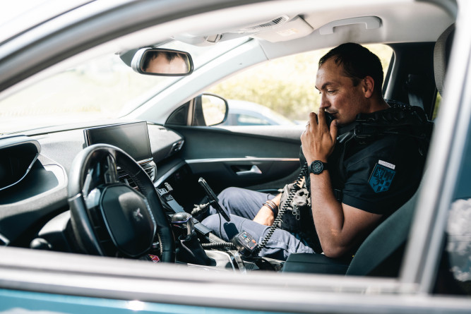 Gendarme parlant à la radio dans son véhicule à l'arrêt, sur le siège passager.