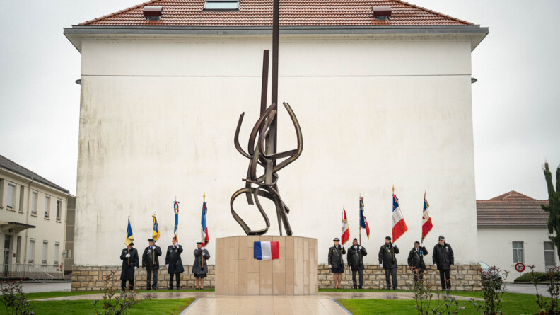 Neuf personnes posent de part et d'autre d'une sculpture en acier, pos&eacute;e sur un socle de pierres de couleur claire. Elle portent dans leur main un drapeau. Le temps est gris et humide.