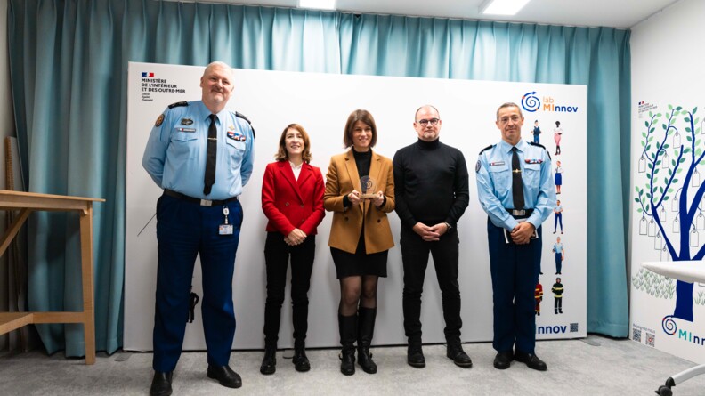 Deux g&eacute;n&eacute;raux de gendarmerie encadrent trois personnes en civil, dont deux femmes. Celle qui se tient au centre tient un troph&eacute;e.