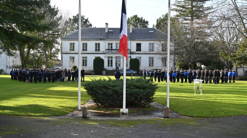 sur une place e herbe des gendarmes et civils alignés, au milieu au premier plan, le drapeau frnaçais