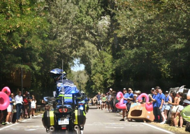 Agrandir l'image Un motocycliste de la gendarmerie roule sur une route par un temps ensoleillé, le long duquel se touve une foule en liesse, lors d'une étape du tour de France 2025