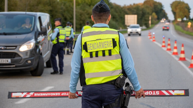 Photo représentant un contrôle routier. Un gendarme, de dos, se tient au premier plan, tandis que ses collègues, au second plan, contrôlent un autre véhicule.