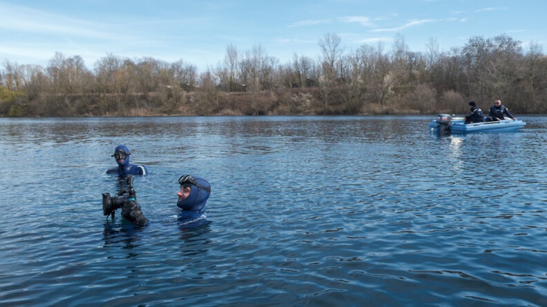 Agrandir l'image Plan large du plan d'eau sur lequel l'on voit en fond, l'un des bateaux de la gendarmerie et en premier plan, deux plongeurs de la gendarmerie entrain de prendre des photos et autres relevées d'enquête.