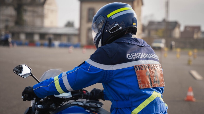 Un motard de la gendarmerie portant un rectangle orange aux lettres noires "moto école 14" s'apprête à réaliser un circuit de type plateau