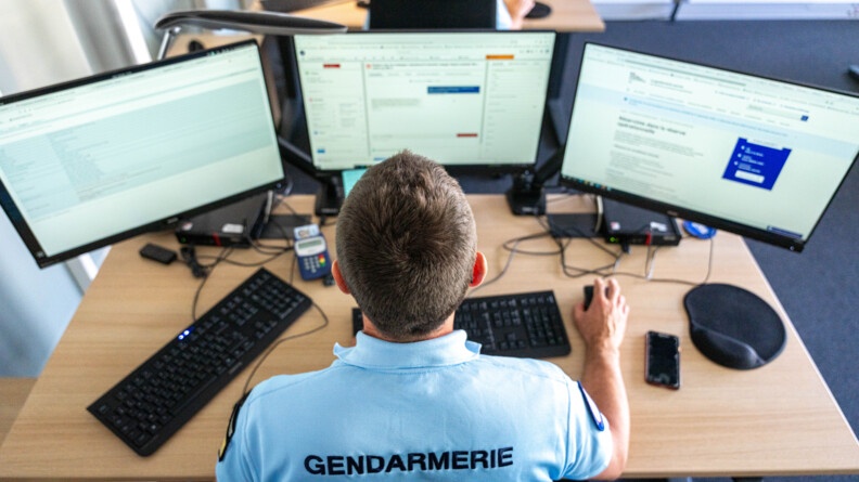 Agrandir l'image Vue en plongée d'un gendarme à son bureau face à trois écrans