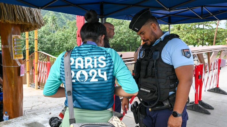 Un gendarme controle une femme au t-shirt vert et bleu Paris 2024 sous une tonnelle bleue