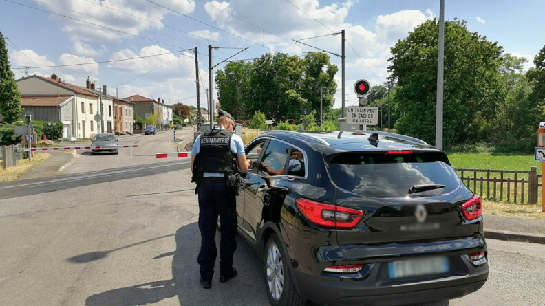 Un gendarme, vu de dos, dispense des conseils de pr&eacute;vention au conducteur d'un v&eacute;hicule noir arr&ecirc;t&eacute; &agrave; un passage &agrave; niveau, dont les barri&egrave;res sont baiss&eacute;es. Au second plan, un second v&eacute;hicule est arr&ecirc;t&eacute; de l'autre c&ocirc;t&eacute; du passage &agrave; niveau.