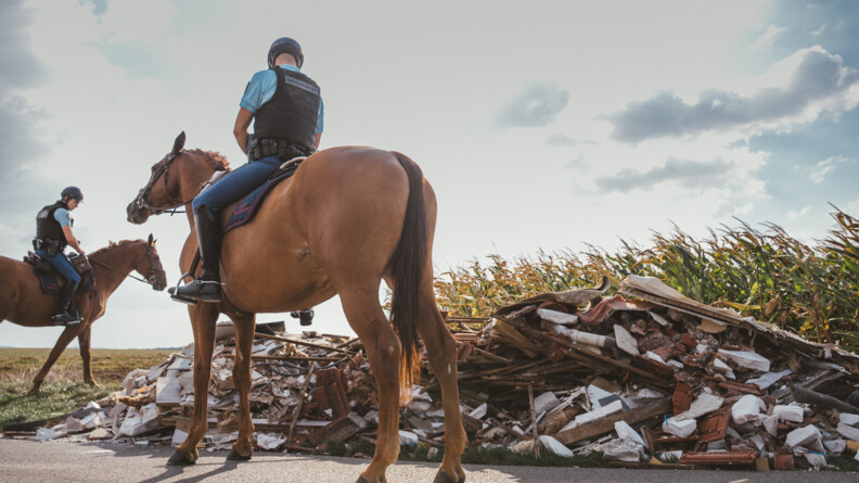Deux gendarmes à cheval auprès dun' dépot de déchets le long d'un rout et d'un champ