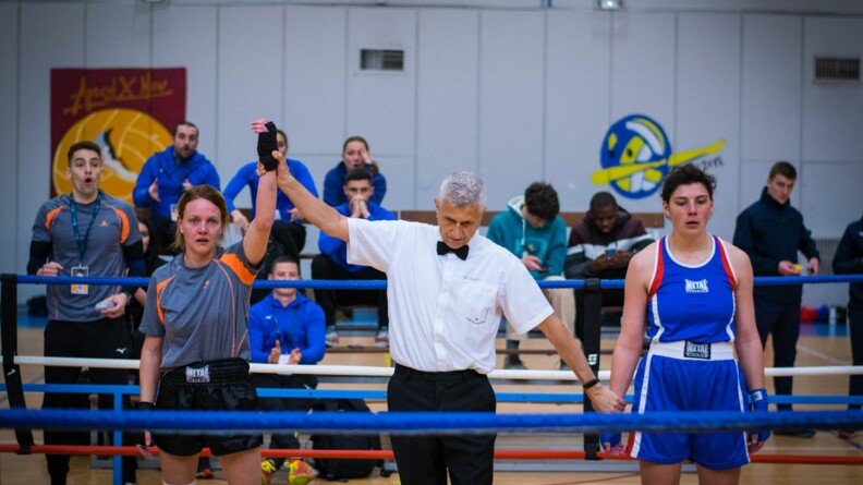 Epreuve de boxe. Sur le ring, en int&eacute;rieur, l'arbitre d&eacute;clare vainqueur une &eacute;l&egrave;ve de l'EOGN habill&eacute;e en gris.