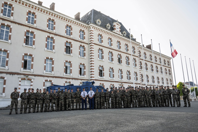 Agrandir l'image Groupe de militaires, alignés côte à côte, devant un grand bâtiment en pierres beiges. Un draperau française flotte devant la façade.