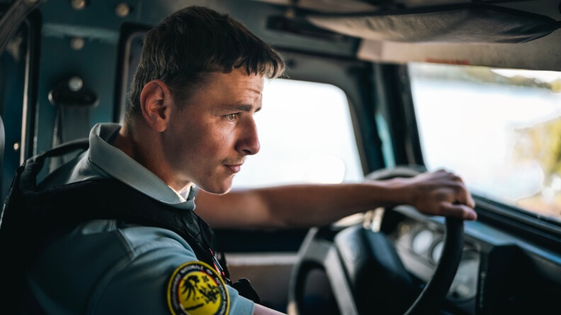 Un gendarme portant un gilet pare balles noir la main gauche sur le volant &agrave; l'int&eacute;rieur d'un v&eacute;hicule bleu