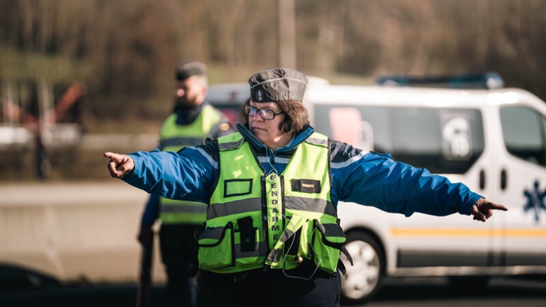 Agrandir l'image Une femme gendarme, au niveau d'un péage autoroutier, fait un signe de la main à un automobiliste, lui itimant de s'arrêter