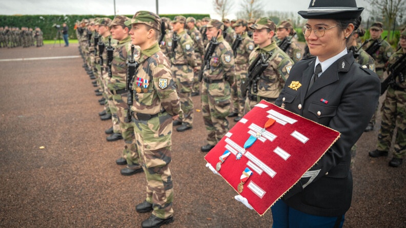 Une gendarme tient un coussin rouge sur lequel sont dispos&eacute;es des d&eacute;corations. A ses c&ocirc;tes se tiennent des &eacute;l&egrave;ves gendarmes en tenue militaire kakie.