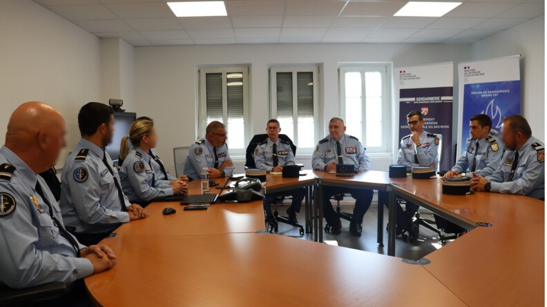Neuf gendarmes, dont une femme, en tenue d'état-major, assis autour d'une table ronde.