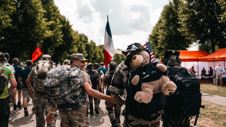 Agrandir l'image Plussieurs militaires en tenue kakie, marchent ensemble. Ils sont photographiés de dos. Un drapeau français émerge du groupe. Un gros ours en peluche est accroché au sac de l'un des militaires.
