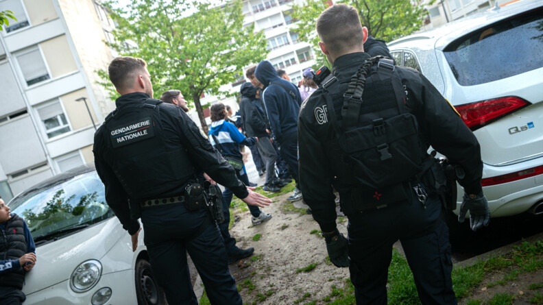 Agrandir l'image Des gendarmes se tiennent debout, autour d'un groupe de jeunes, au niveau du parking d'un ensemble d'immeuble d'habitations.
