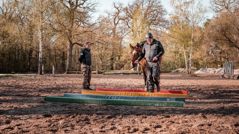 Christophe, au centre, participant au stage Cent'Or, guide son cheval sur un parcours d'embûches, sous le regard de son accompagnante, à gauche.
