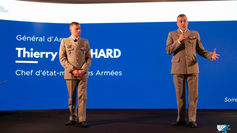 Deux g&eacute;n&eacute;raux en vareuse beige, sur une sc&egrave;ne noire, avec en arri&egrave;re-plan, sur fond bleu, l'inscription "G&eacute;n&eacute;ral d'arm&eacute;e Thierry Burkhard, chef d'&eacute;tat-major des Arm&eacute;es".  A gauche, le g&eacute;n&eacute;ral Paul Sanzey, debout, les mains crois&eacute;es devant lui ; &agrave; droite, s'exprimant au micro, le g&eacute;n&eacute;ral d'arm&eacute;e Thierry Burkhard.