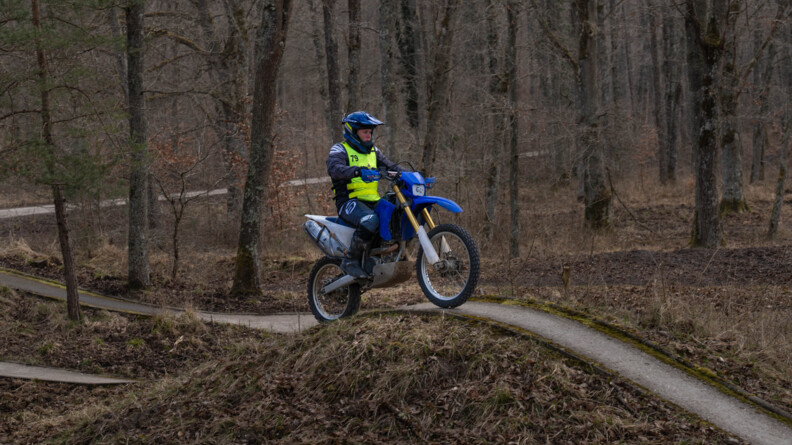 Une motarde de la gendarmerie sur une moto cross roule sur une étroite bande de goudron dans la forêt aux couleurs rousses
