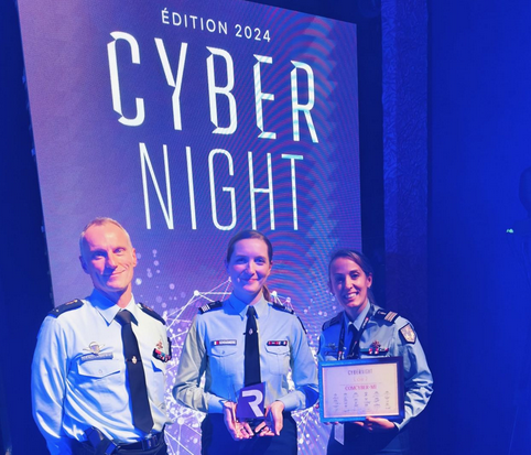 Trois gendarmes (deux hommes et une femmes) posent fièrement, un prix à la main, deavtn un kakémono portant la mention Edition 2024 - CYBERNIGHT