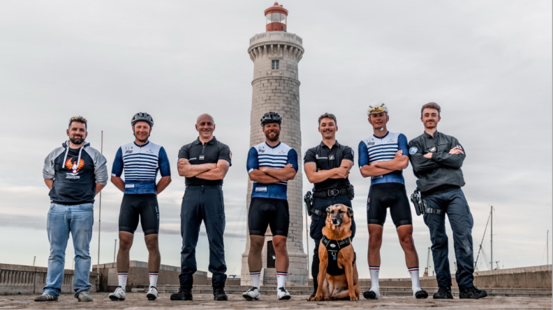 Sept hommes dont trois gendarmes en noir, sur un pont au bout duquel se trouve un phare blanc et vert, avec un chien malinois assis devant le troisième à partir de la la droite
