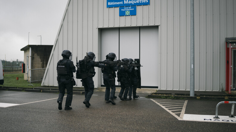 Photo en extérieur de la progression d'une colonne de militaire du PSPG entrain d'avancer en direction d'un batiment blanc.
