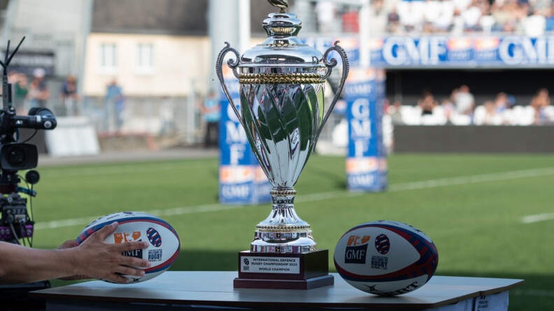 Trophée de la coupe du Monde militaire entouré de deux ballons de rugby