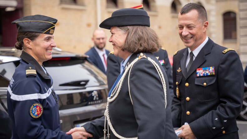 La commandante de la KMar (Royal Netherlands Marechaussee) salue une femme colonel de la gendarmerie nationale dans une cour. Les deux femmes sont en uniforme et se sourient.