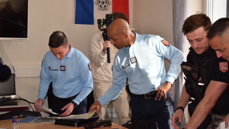 Trois gendarmes penchés sur des cartes et radio autour d'une table