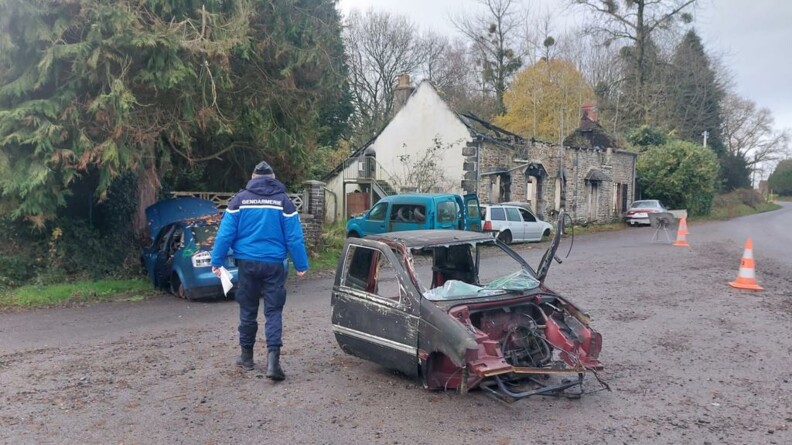 Un gendarme de dos se déplace au milieu d'un champ de véhicules épaves