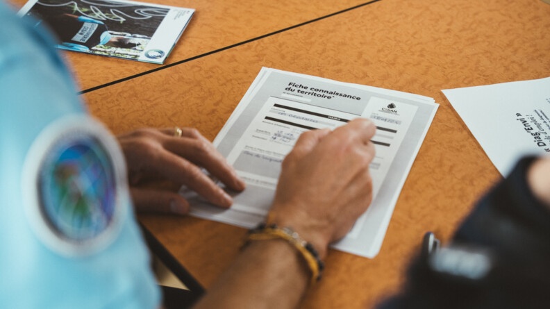 Sur une table vue sur le bras et la main d'un gendamre remplissant un document