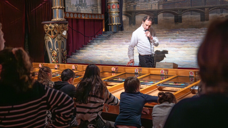 Nous voyons des enfants jouer aux anciens jeux de f&ecirc;te foraine avec un commentateur au micro qui explique le jeu.