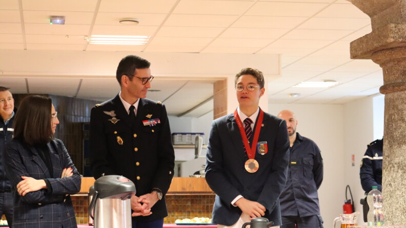 Photo du nageur Hector Denayer, revêtant une médaille autour de cou, entouré de gendarmes et d'une femme civile