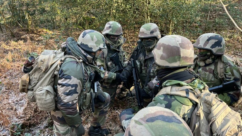 Groupe de 6 gendarmes accroupis, en cercle, dans la for&ecirc;t entrain d'&eacute;changer des consignes.