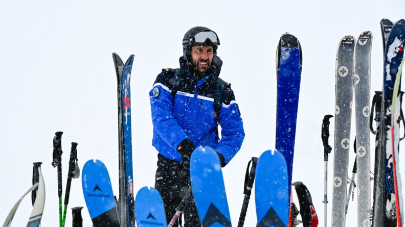 deriière des skis debout, un gendarme  coiffé d'un casque de ski sous la neige