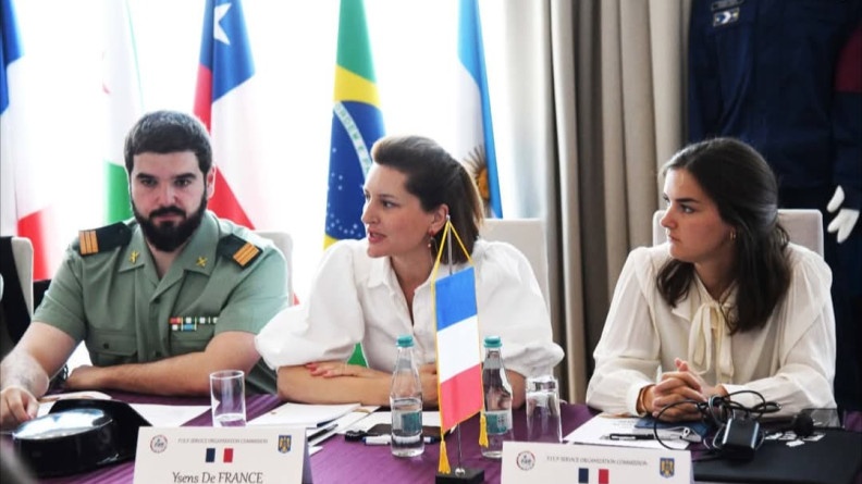 Agrandir l'image En femme en blanc est en train de parler. Derrière elle se trouve des drapeaux de plusieurs pays dont le Brésil. A côté d'elle se trouve ( à sa droite), une autre jeune femme en blanc, (aà sa gauche), un gendarme de la Guardia Civil espagnol.