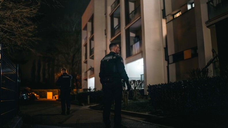 Deux gendarmes patrouillent au pied d'un immeuble. Il fait toujours nuit et sombre.
