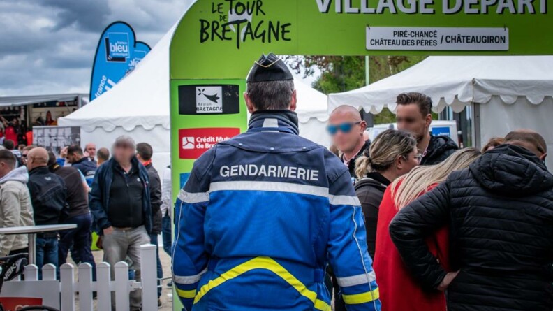 Gendarme vu de dos, au milieu du public, face au kakémono du village de départ.