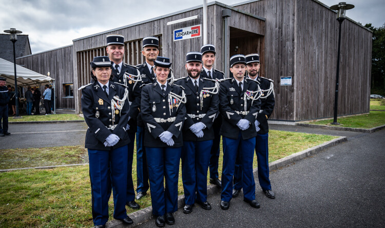 Huit gendarmes en uniforme se tiennent debout, regroup&eacute;s, devant un b&acirc;timent en bois, sur lequel on apercoit une pancarte aux couleurs bleu, blanc, rouge, portant l'inscription Gendarmerie.