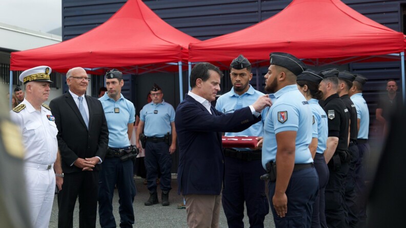 Le ministre des outre-mer, Manuel  Valls, remet une décoration à un gendarme que l'on voit de profil.
