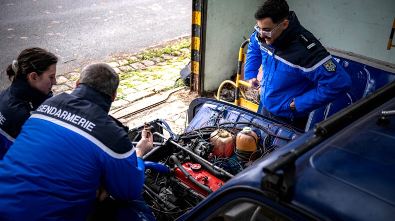 Trois gendarmes autour d'une 4L dont le capot est ouvert, moteur visible