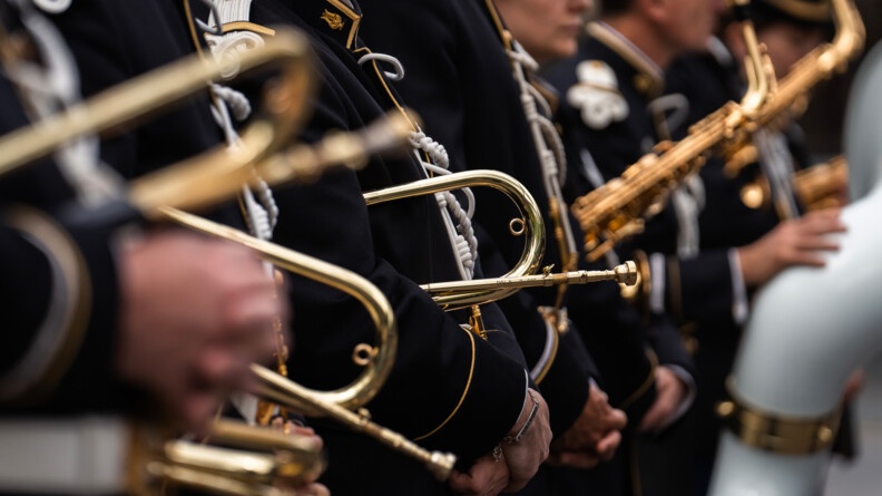 Photo prise lors d'une cérémonie officielle. On aperçoit les bras de militaires en uniforme bleu marine, avec leur instrument de musique dans les mains.