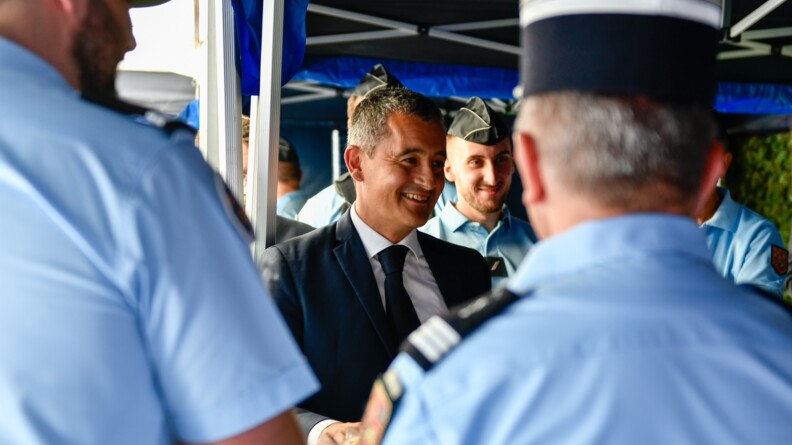 Au premier plan, deux gendarmes vus de dos. Face &agrave; eux, G&eacute;rald Darmanin, souriant. D'autres gendarmes de face en arri&egrave;re-plan.