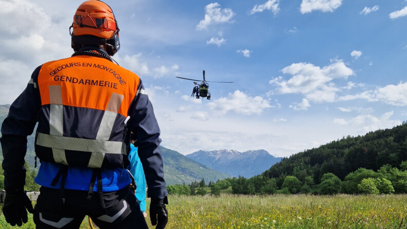 Un gendarme de PGHM attend le treuillage d'un hélicoptère au-dessus de la vallée. Deux hommes apprêtent à descendre
