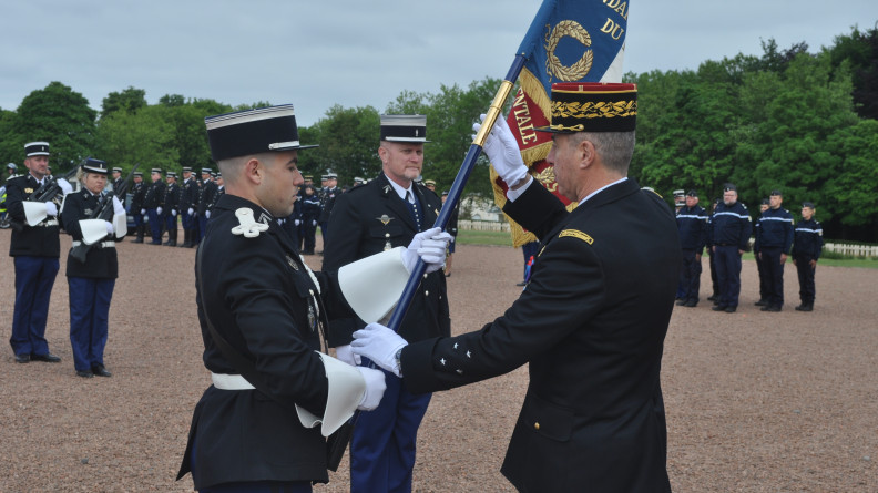 Remise d'un drapeau par un général à un colonel de gendarmerie lors d'une cérémonie militaire.