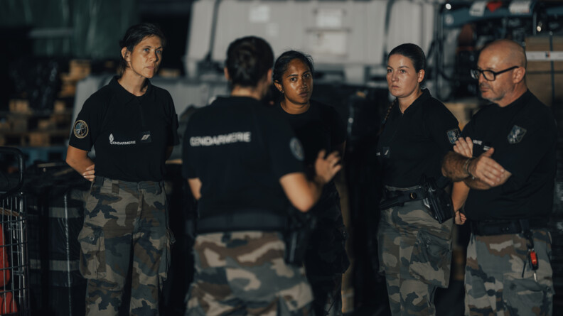Une femme gendarme, métisse, se tient debout au milieu d'un groupe de gendarmes.