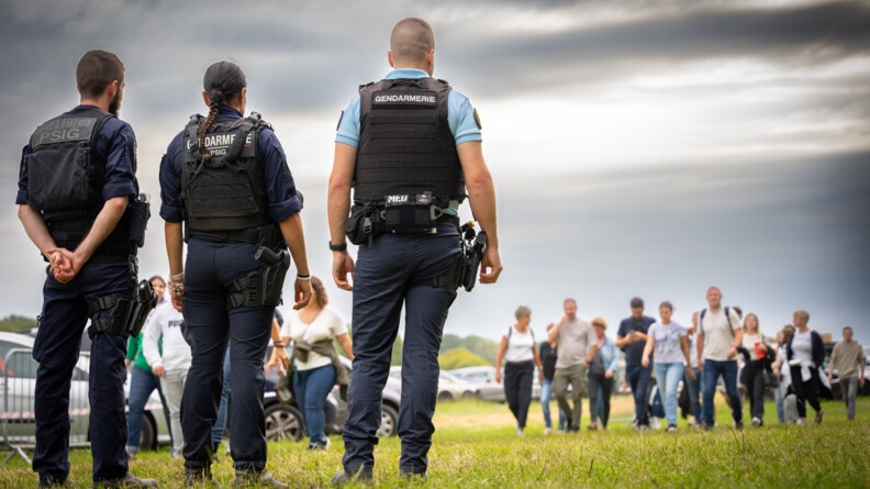 Agrandir l'image Trois gendarmes de dos surveillent l'arrivée des spectateurs sur le parking aux abords du château de Chambord.