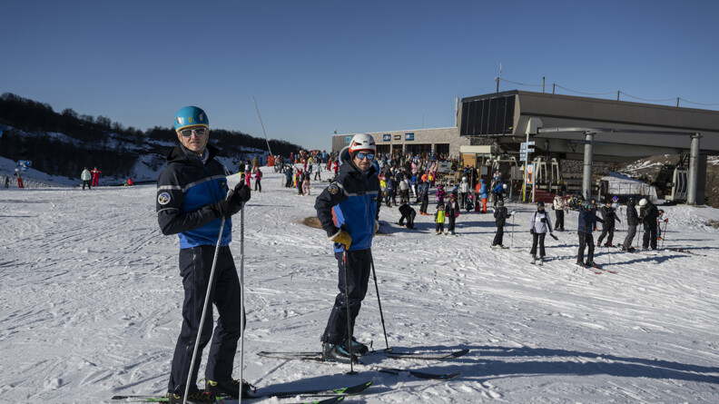 Deux gendarmes sur des skis devant une station enneigée et la foule de skieurs sous un ciel bleu