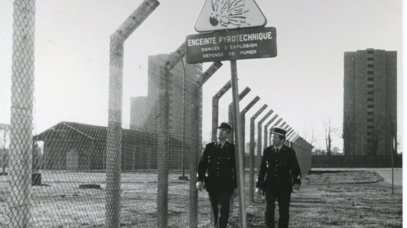 Sur une photo en noir et blanc, deux gendarmes marchent le long d'un grillage repr&eacute;sentant de toute &eacute;vidence la bordure d'un site militaire dont ils ont en charge la s&eacute;curisation.