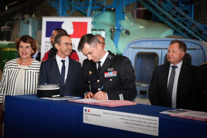Un colonel de gendarmerie signe une convention sur une table recouverte d'un tissu bleu. A sa droite se tiennent le ministre de l'intérieur, Bruno, Retailleau, et la ministre de l’Agriculture et de la Souveraineté alimentaire, Annie Gennevrard